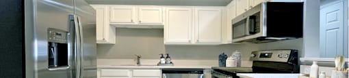 Spacious bright white kitchen with white cabinets, stainless steel appliances, side-by-side refrigerator, and tiled floor at Prestonbridge Apartments in North Dallas