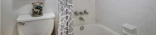 Bright white bathroom with white shower tiles at Woodlake Oaks Apartments in Houston