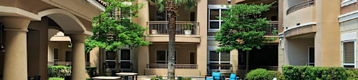 Luxury apartments with palm trees, spacious sundeck with poolside lounge chairs, grilling station, ping-pong table, and fountains at Villa Piana Apartments in Dallas