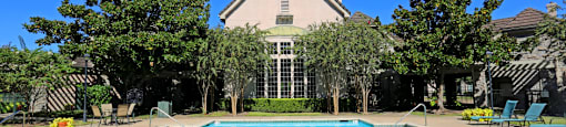 Luxury resort-style swimming pool with poolside lounges chairs, beautiful landscaping, lush landscaping and scenic views at Village on the Parkway Apartments.