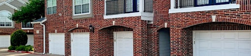 Luxury apartments in a gated community with red brick exteriors and attached garages at Prestonbridge Apartments in North Dallas