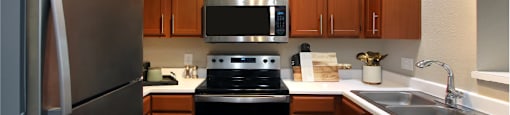 Luxury kitchen with wood plank floors, stainless steel appliances, honey brown cabinets, and white countertops at Lenox Village Apartments