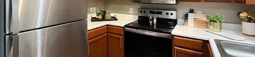 Luxury kitchen with wood plank floors, stainless steel appliances, honey brown cabinets, and white countertops at Lenox Village Apartments