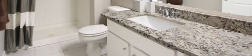 Spacious luxury bathroom with white cabinets, granite countertops, gray wall color, porcelain tile floor, and walk-in shower at Breckenridge Apartments