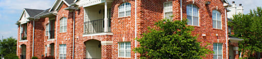 Luxury apartments with red brick exterior, spacious balconies, lush landscaping, park-like setting, and scenic views at Lenox Village Apartments in Lincoln, Nebraska
