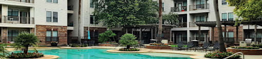 Luxury swimming pool with cabanas, poolside lounges, grilling stations, palm trees and beautiful landscaping at The Voss Apartments in Houston.