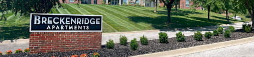 a sign apartments in front of a lawn and trees