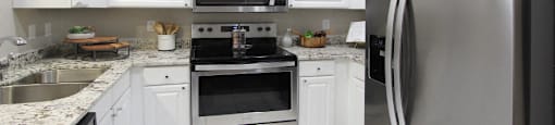 Luxury apartments with granite countertops, white cabinets, stainless steel appliances, and side-by-side refrigerator at TurtleCreek apartments in West Des Moines, Iowa