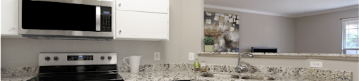 Spacious kitchen with white cabinets, granite countertops, stainless steel appliances, serving bars, and porcelain tile floors at Breckenridge Apartments in southwest Omaha, Nebraska