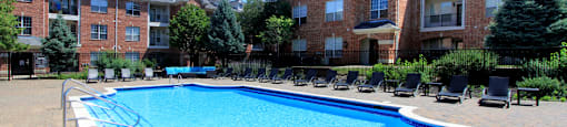 Luxury apartments with red brick exterior, huge swimming pool, poolside lounge chairs, grilling station, and lush landscaping at TurtleCreek apartments in West Des Moines, Iowa