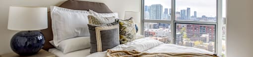 a bedroom with a large window and a bed with white sheets and pillows