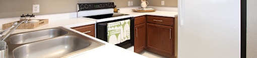 Spacious u-shaped kitchen with lots of cabinet space, lots of counter space, porcelain tile floor, and rich brown toned cabinets at The Biltmore Apartments in Omaha, Nebraska
