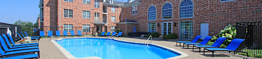 an outdoor pool with blue chairs and a brick building