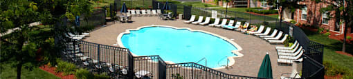 an outdoor pool with lounge chairs and umbrellas in front of a brick building