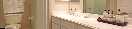 Luxury apartments with white cabinets, linen closet, extra cabinet space, cultured marble vanity, built-in vanity, roman tub with glass door and shower, and porcelain tiled floor at The Biltmore Apartments in Omaha, Nebraska