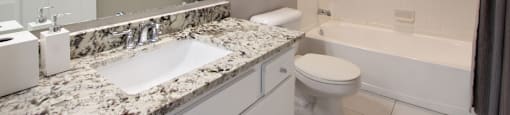 Spacious luxury bathroom with white cabinets, granite countertops, gray wall color, porcelain tile floor, soaking tub and tiled shower at Breckenridge Apartments in Omaha, Nebraska