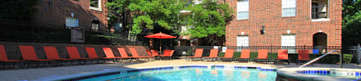 Gated community near the Galleria with brick exteriors, lush landscaping, two swimming pools with poolside lounge chairs, spa, and sauna at The Dorchester Apartments in Houston.