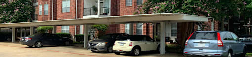 Luxury apartments in a gated community with covered car ports and red brick exteriors at Tuscany Oaks Apartments in Houston.