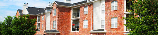 Luxury apartments with red brick exterior, attached garages, lush landscaping, and scenic views at Lenox Village Apartments in Lincoln, Nebraska
