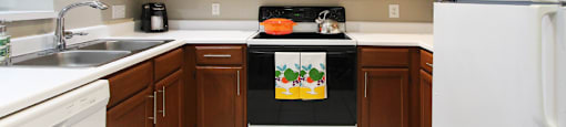 Luxury apartments with honey brown cabinets, tiled floors, white countertops, and u-shaped kitchen at Lenox Village Apartments in Lincoln, Nebraska