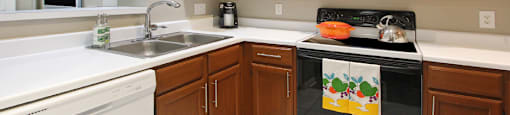 Luxury apartments with honey brown cabinets, tiled floors, white countertops, and u-shaped kitchen at Lenox Village Apartments in Lincoln, Nebraska