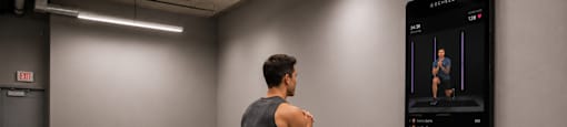 A man is running in a gym with a digital display showing his workout progress.