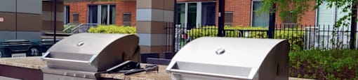 Two silver barbecue grills on a striped concrete surface.