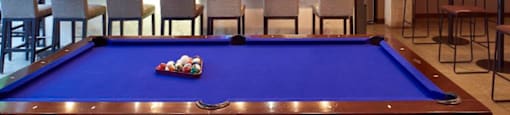 A pool table with a blue cloth and a television mounted on the wall.