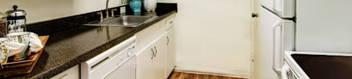 Apartments near the Galleria with bright white kitchens, black countertops, and wood plank flooring at Plantation apartments in Houston.