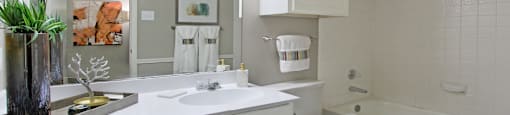 Spacious bathroom with white cabinets and white porcelain tile at Preston Village Apartments in North Dallas