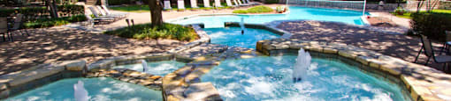 Luxury apartments with beautiful fountains, beautiful landscaping, swimming pool with poolside lounge chairs, and scenic views at Preston Village Apartments in north Dallas