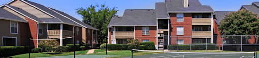 Luxury apartments with tennis court, red brick exteriors, beautiful landscaping, and spacious balconies at Preston Village Apartments in North Dallas