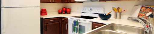 Spacious kitchen with honey brown toned cabinets, lots of counter space, white appliances, tile floor and recessed ceiling at Tuscany Oaks Apartments in Houston