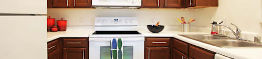 Spacious kitchen with honey brown toned cabinets, lots of counter space, white appliances, tile floor and recessed ceiling at Tuscany Oaks Apartments in Houston