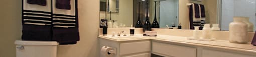 Spacious bathroom with oval soaking tub with glass enclosure, cultured marble vanity, glass shower, and built-in vanity at Tuscany Oaks Apartments in Houston.