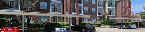 Luxury apartments in a gated community with covered carports and red brick exteriors at Tuscany Oaks Apartments in Houston.