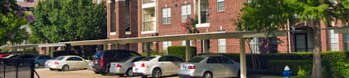 Luxury apartments in a gated community with covered carports and red brick exteriors at Tuscany Oaks Apartments in Houston.