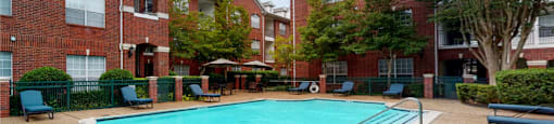 Luxury apartments with red brick exteriors, large swimming pool with spacious sundeck, grill, beautiful landscaping, lush landscaping, chaste trees, and pool-side lounge seating at Tuscany Apartments in Houston.