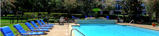 Luxury resort-style swimming pool with fountain, poolside lounges chairs, beautiful landscaping, lush landscaping and scenic views at Village on the Parkway Apartments.