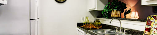 Bright white kitchens with black countertops and wood plank floors at Waters of Winrock Apartments in Houston