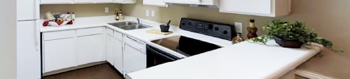 Bright spacious kitchen with white cabinets, breakfast bar, and wood pattern flooring at Woodlake Oaks Apartments in Houston