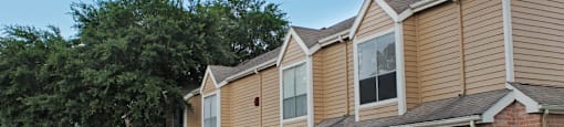 Gated apartment community in the Bayou area of Houston with attached garages, covered parking, 2 swimming pools, lush landscaping, and scenic views at Woodlake Oaks Apartments in Houston.