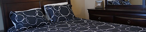 A bed with a black and white patterned comforter sits in a bedroom with a framed word art on the wall.