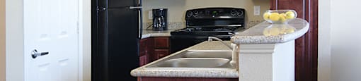 A kitchen with a black refrigerator and brown cabinets.