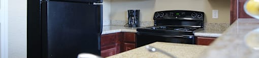 A black refrigerator is in a kitchen with wooden cabinets.