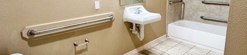 A white toilet sits in a bathroom with a white sink and a white tub.