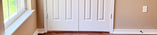 A white door with a black handle is in a room with a window and wooden flooring.
