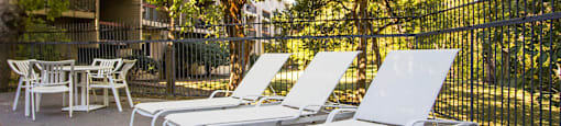 three lounge chairs on a deck in front of a fence and trees