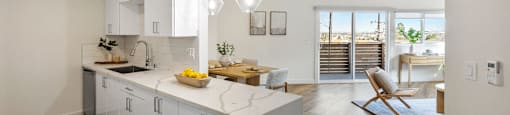 an open kitchen and living room with white cabinets and a marble counter top