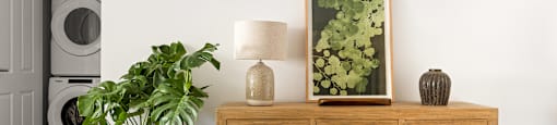 A wooden table with a potted plant, a lamp, a picture, and a bowl on it.